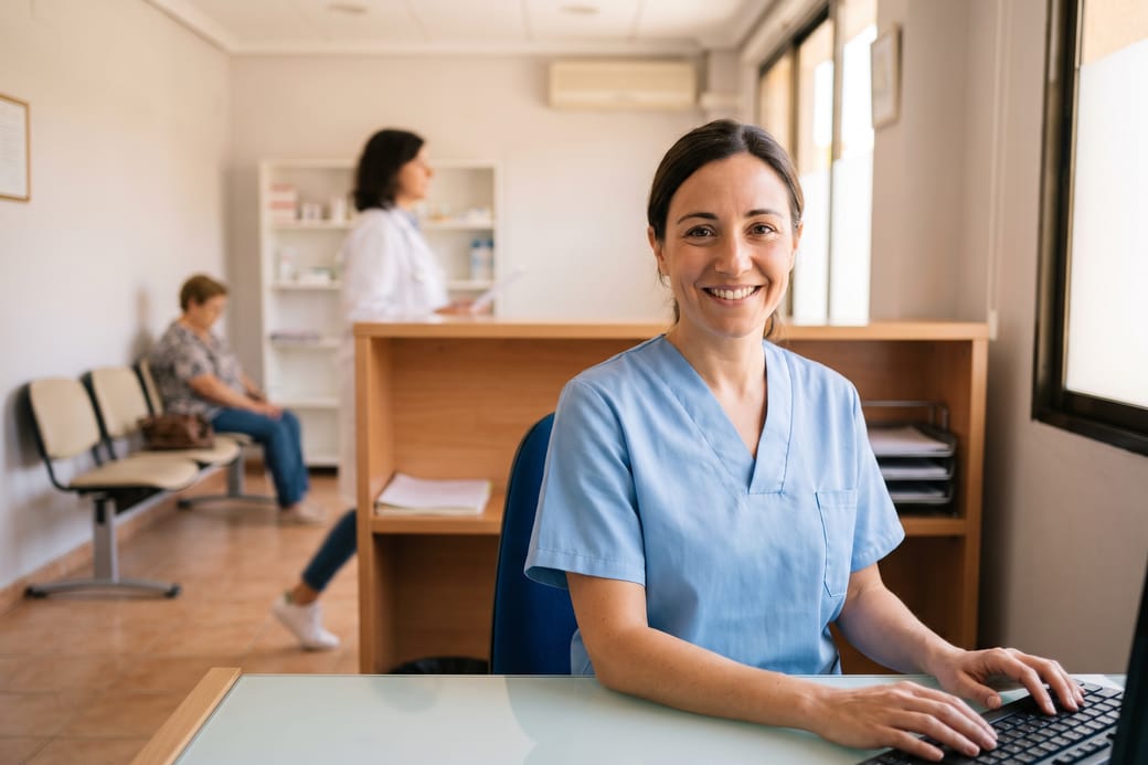 Recepcionista de una clínica, con una paciente esperando detrás