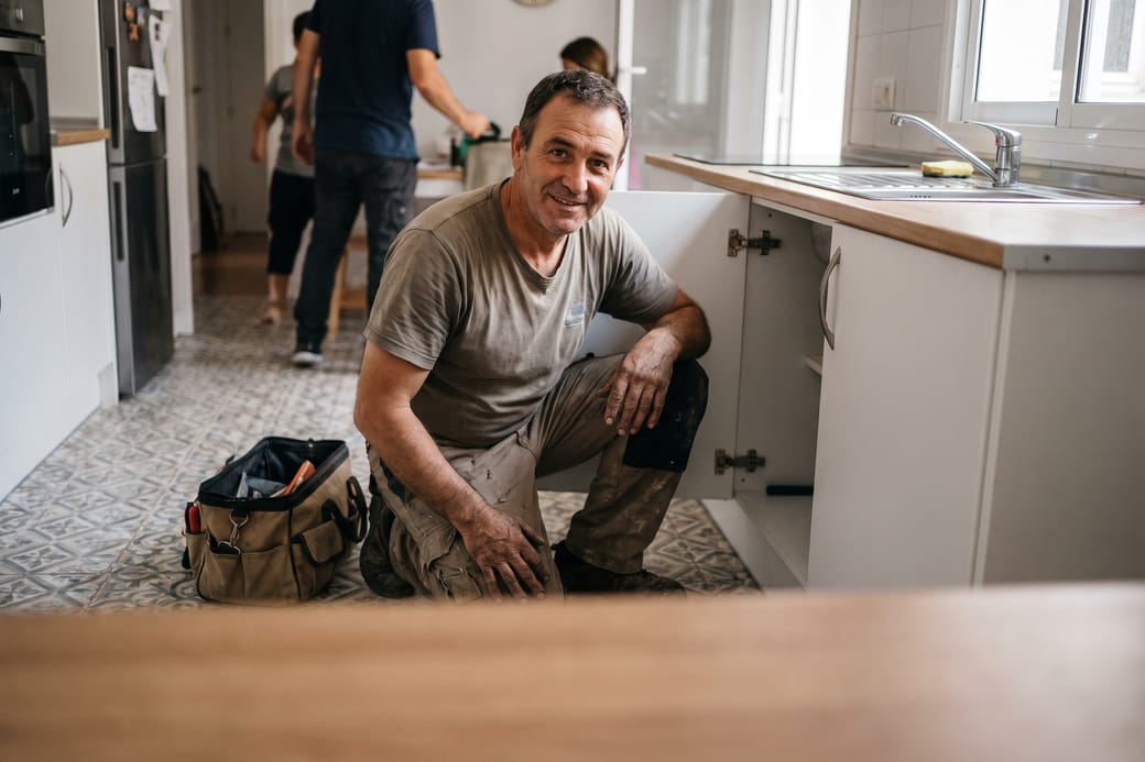 Fontanero agachado junto al mueble del fregadero de una cocina